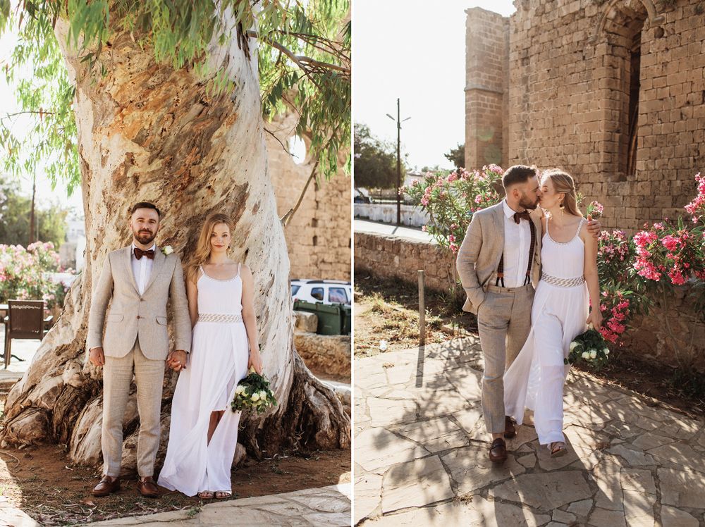 Wedding couple kissing near blooming pink roses beside historic stone church exterior.