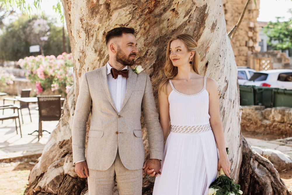 Bride and groom holding hands while standing before a massive ancient tree trunk.