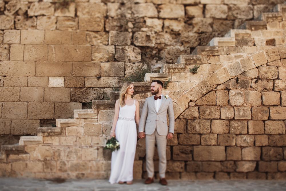 Bride and groom holding hands in front of ancient stone wall with steps during wedding photo session.