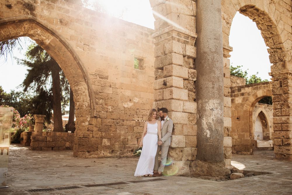 Wedding couple standing together among historic stone ruins with beautiful arch columns.