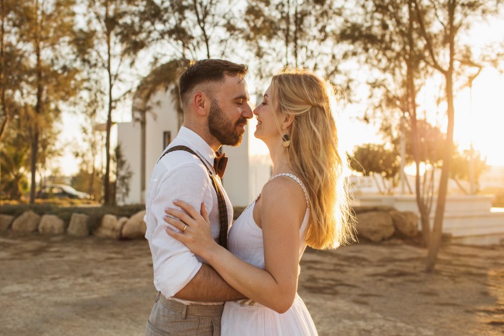 Couple shares a romantic moment face to face bathed in warm golden sunset light outdoors.
