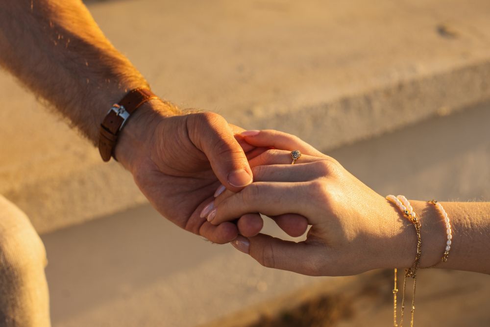 Close-up of bride and groom gently holding hands revealing a watch and delicate gold bracelet.