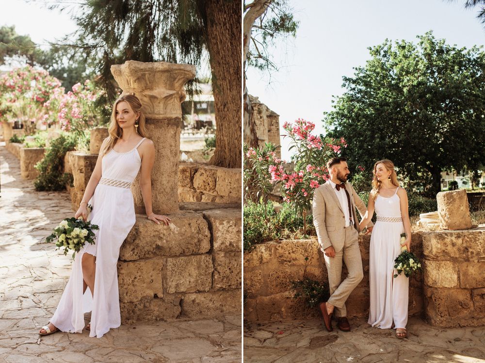 Elegant bride holding bouquet posing beside groom at ancient Mediterranean stone ruins.