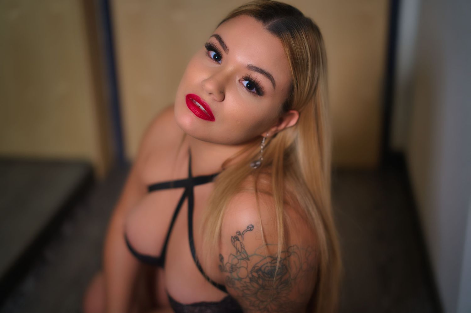 A sensual portrait with dramatic lighting highlighting red lips and a visible tattoo.
