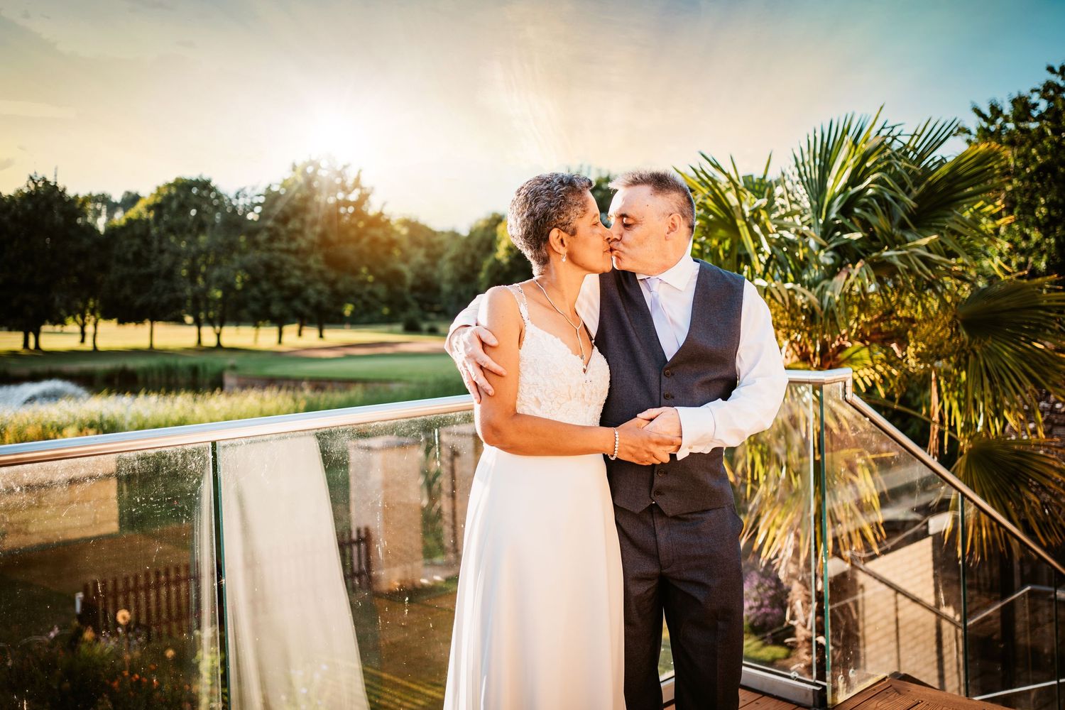 Mature couple mixed race kissing on their wedding day with palm trees and golden sunshine