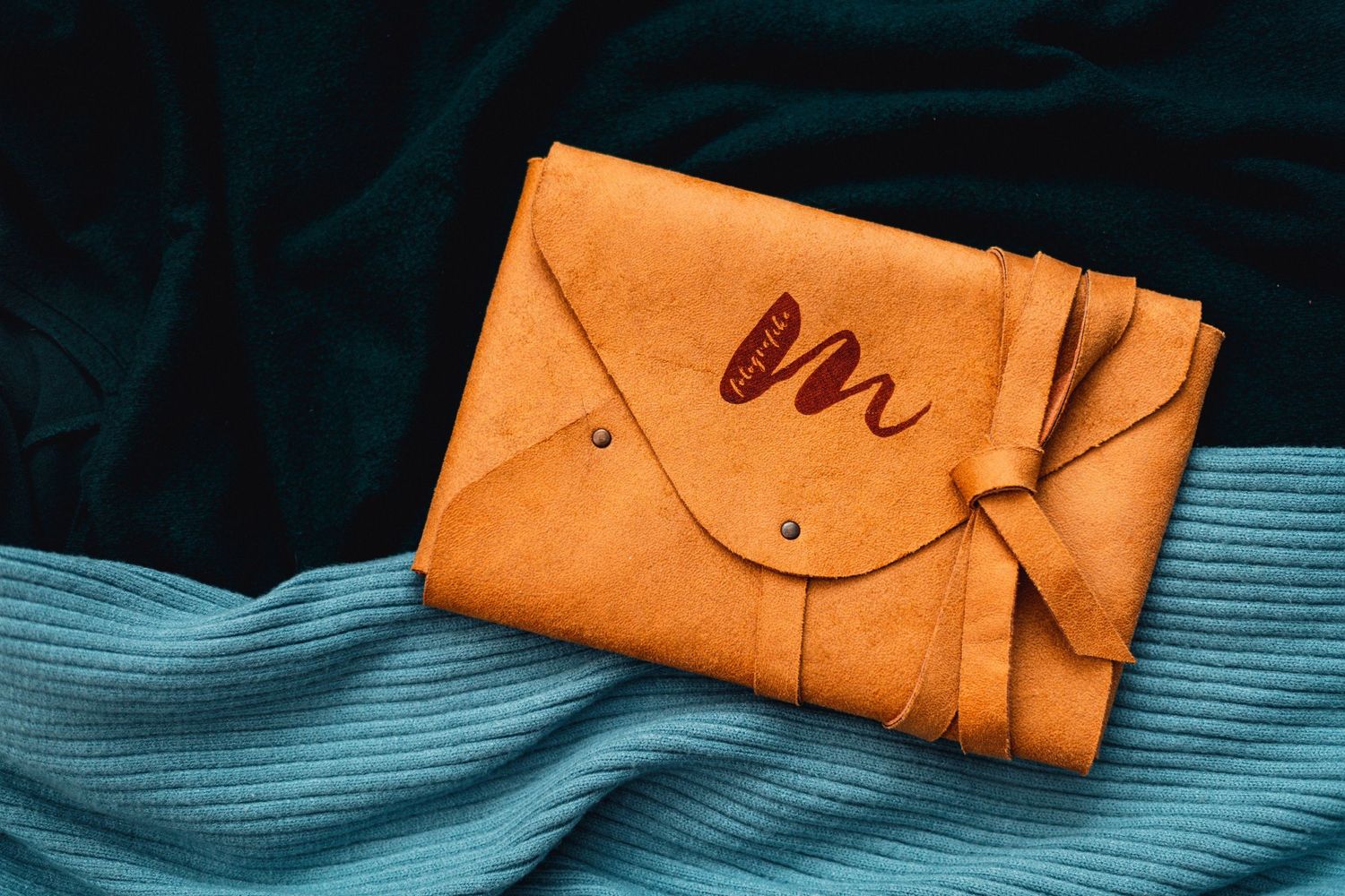 Orange leather photo album cover with decorative stitching on blue textile.