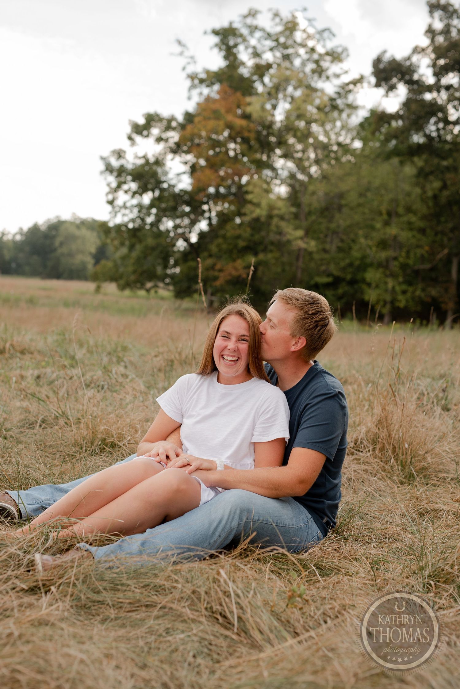 A candid moment of joy between a couple sitting in a sun-drenched field.