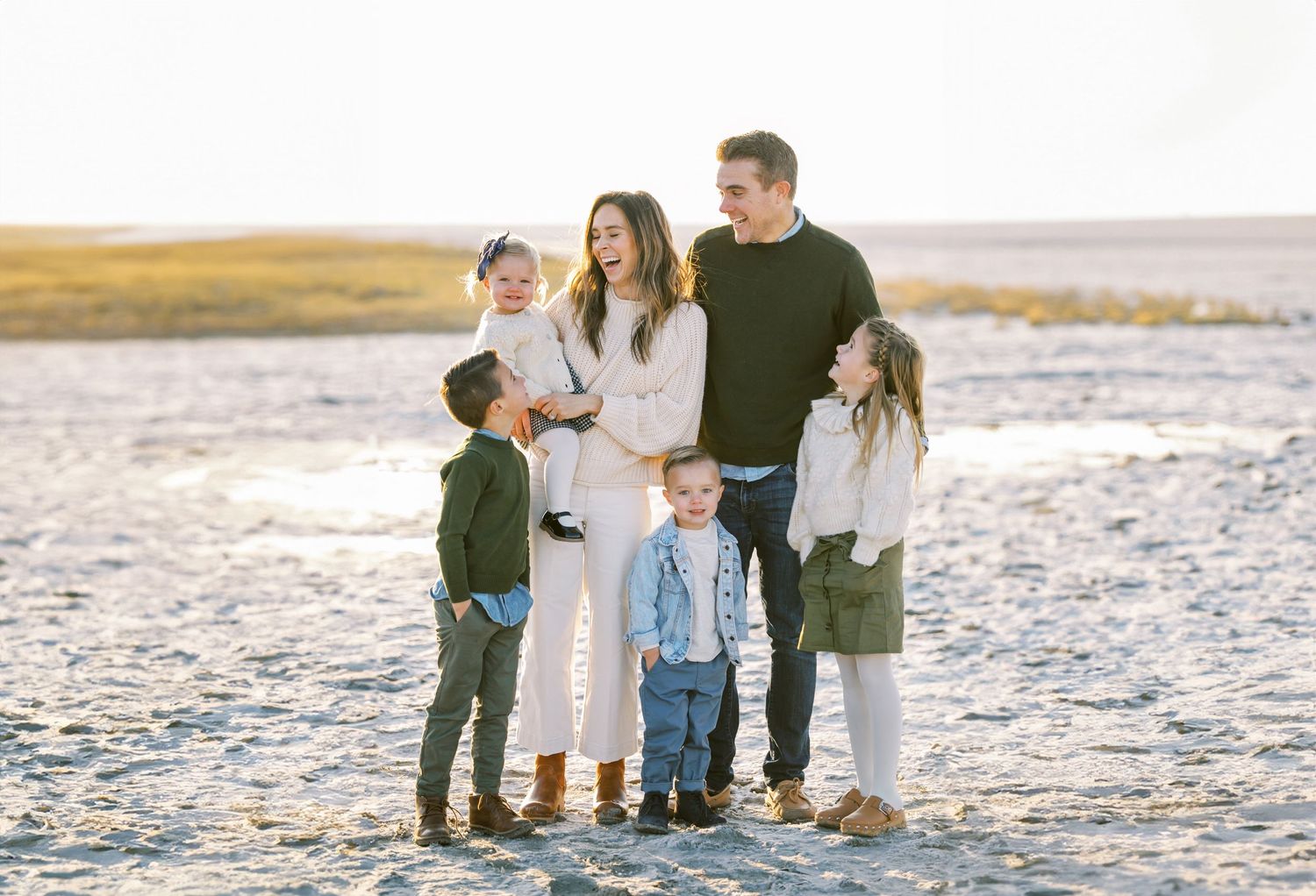 Family of five poses together on sandy beach at sunset.