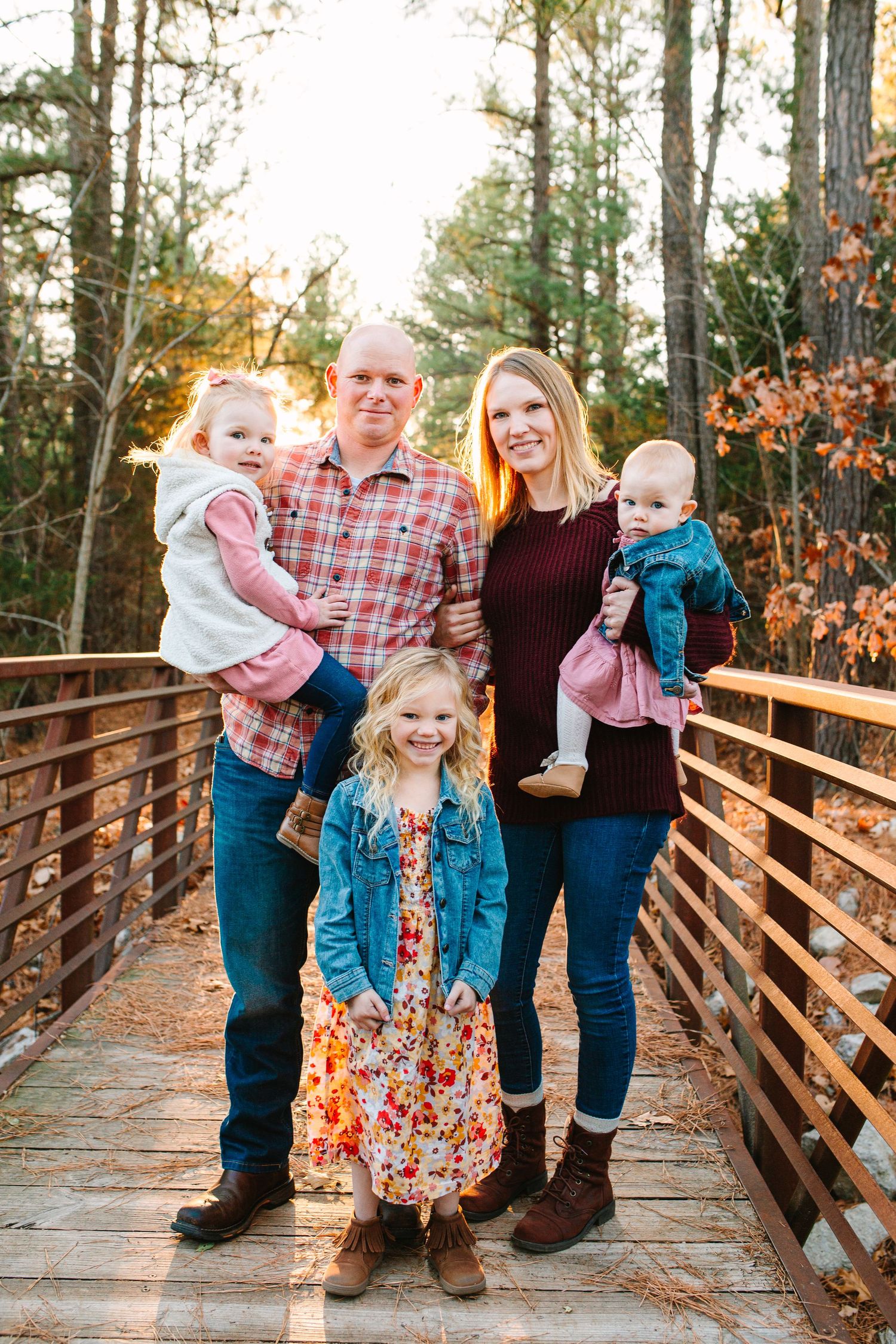 family of 5 stand for their family photo in the middle of a small bridge, where the fall sun is setting behind them