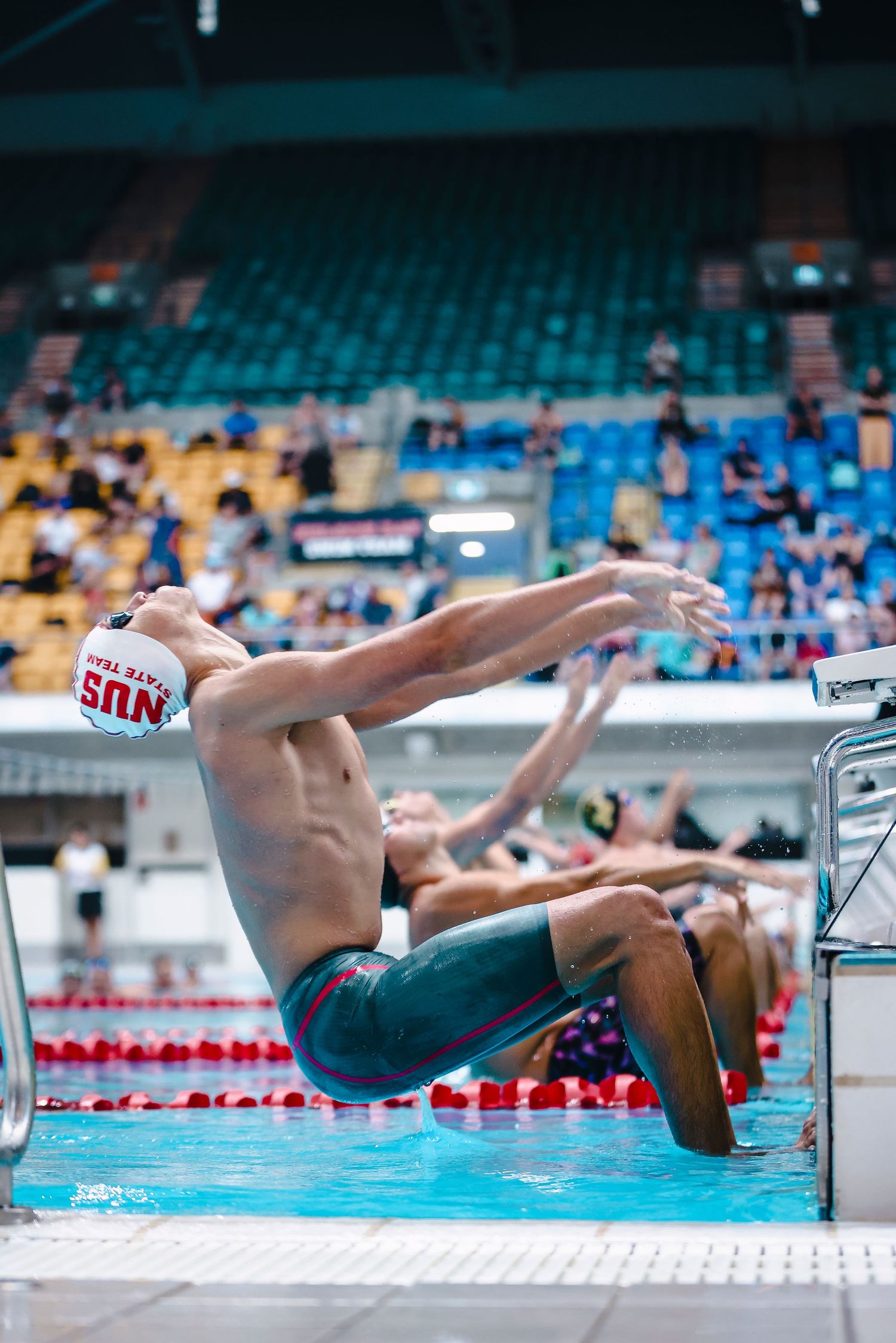 Swimmer diving into pool from starting block during competition.
