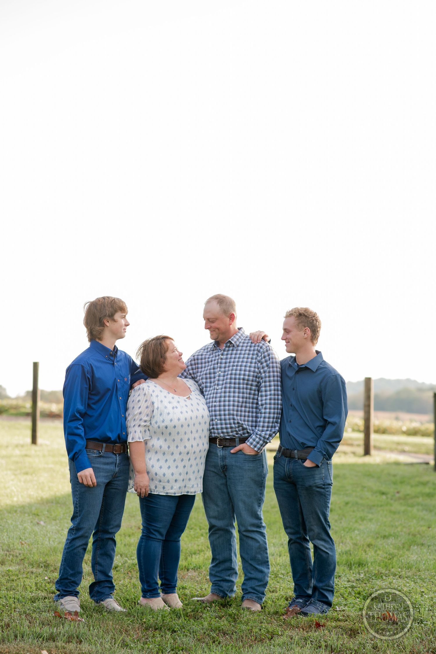 A casual outdoor family portrait with four people standing together against a rural backdrop.
