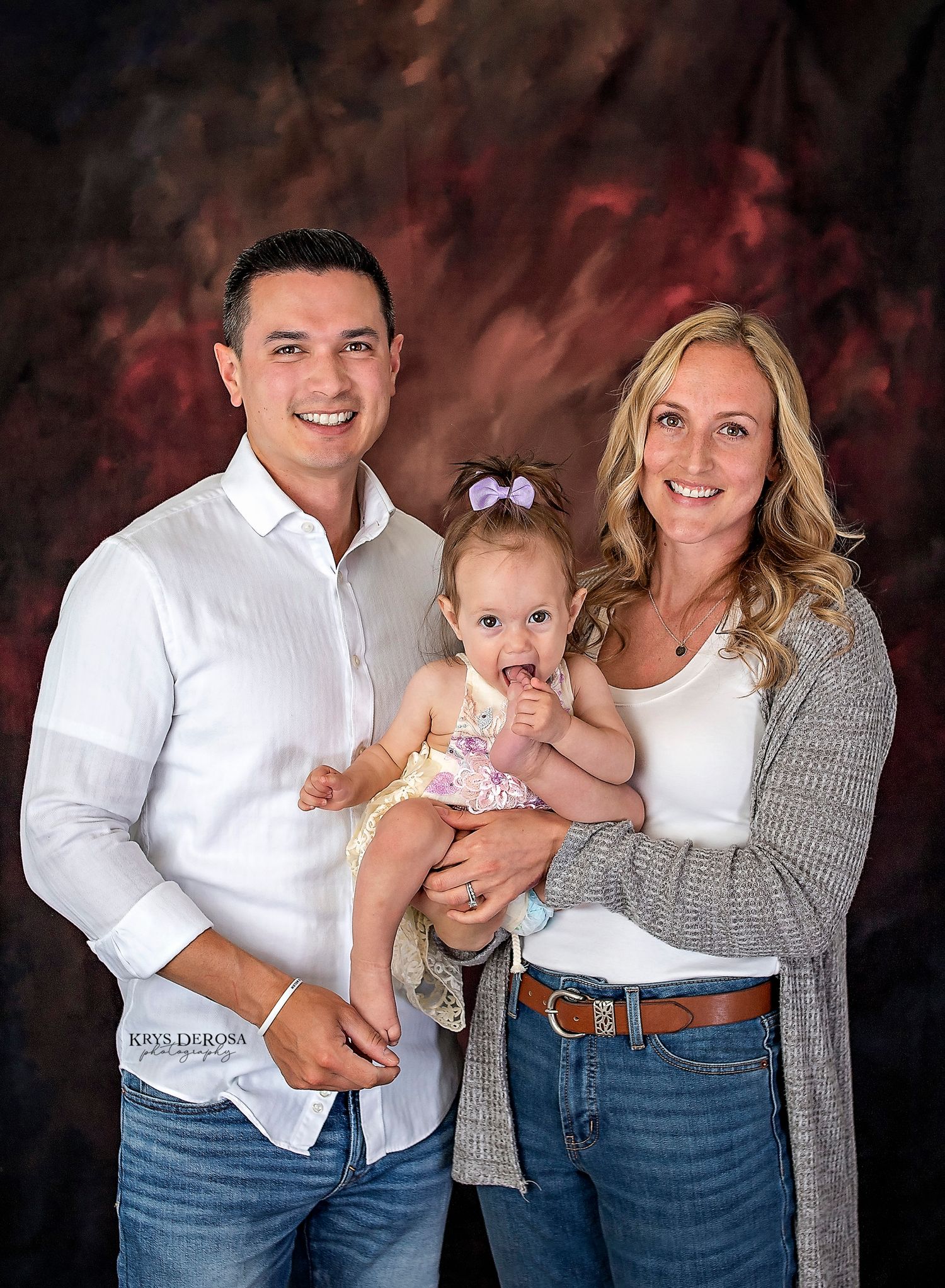Professional studio family portrait with dramatic burgundy background.