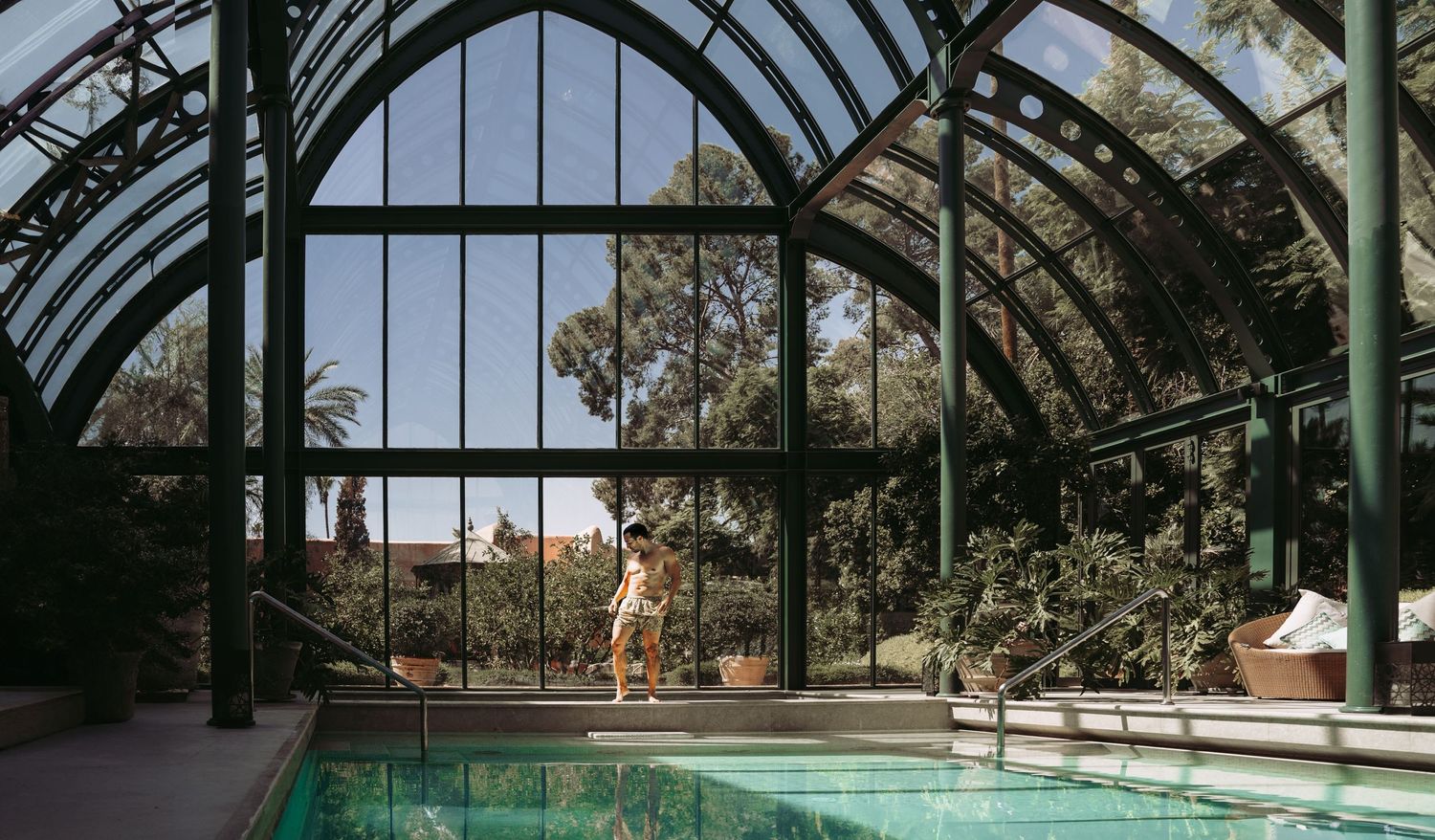 Indoor swimming pool under an elegant arched glass conservatory roof with natural lighting.