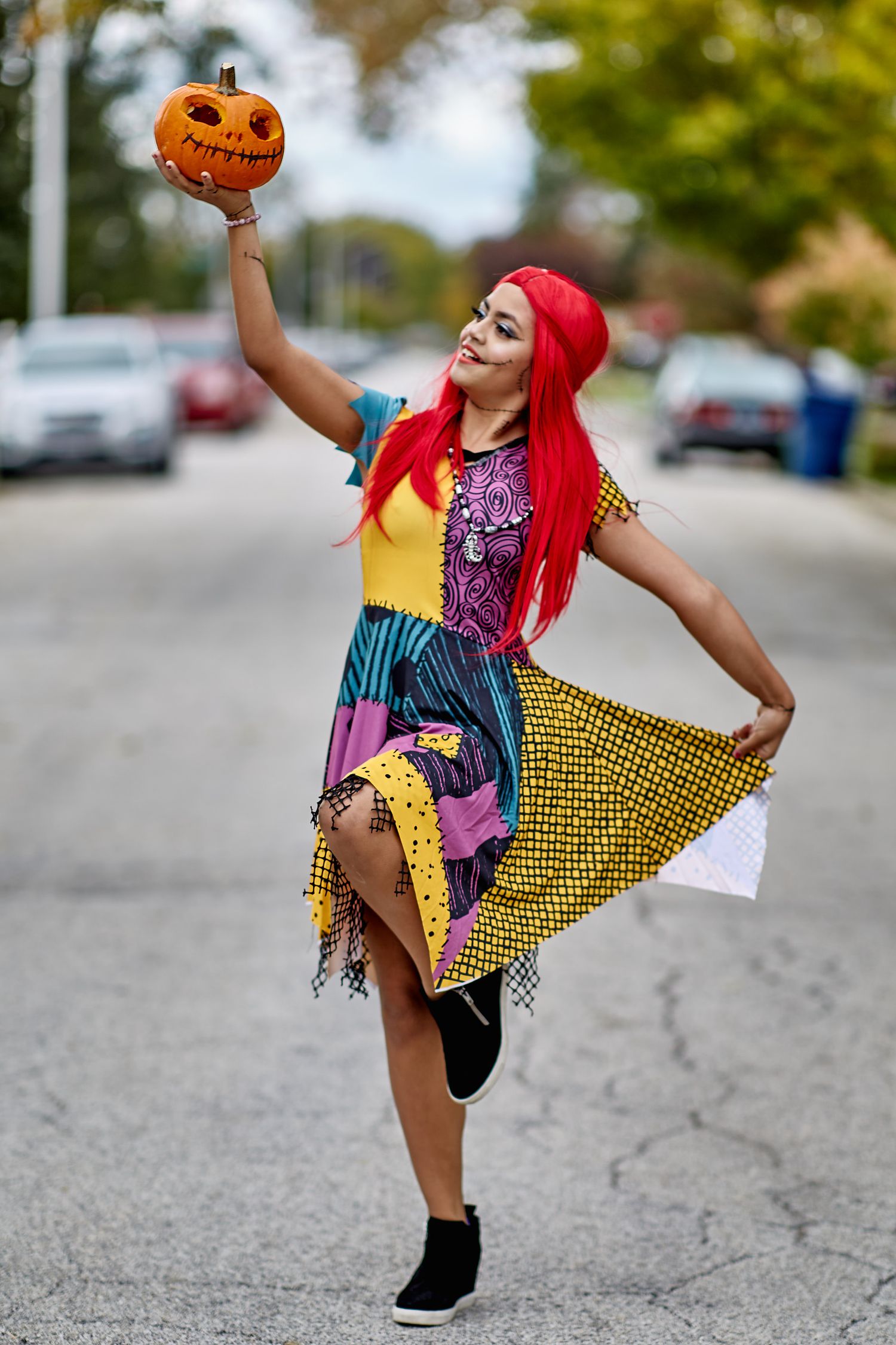 Colorful patchwork dress and bright red hair complement a playful pose with a Halloween pumpkin.