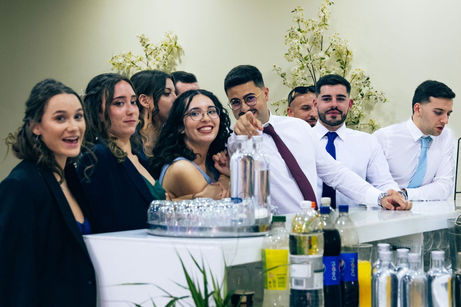 Large group celebrating at an elegant event with drinks and decorative floral arrangements.