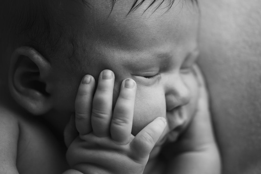 Black and white image of newborn baby girl with hand on her cheek.