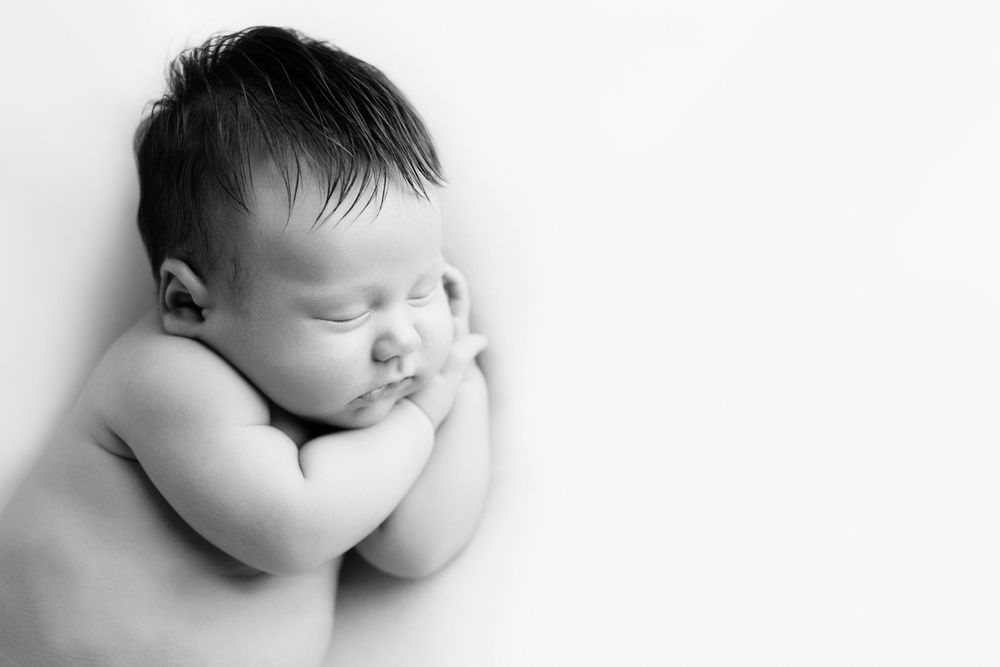 Newborn baby girl on a white blanket laying on her side with both hands under her head.