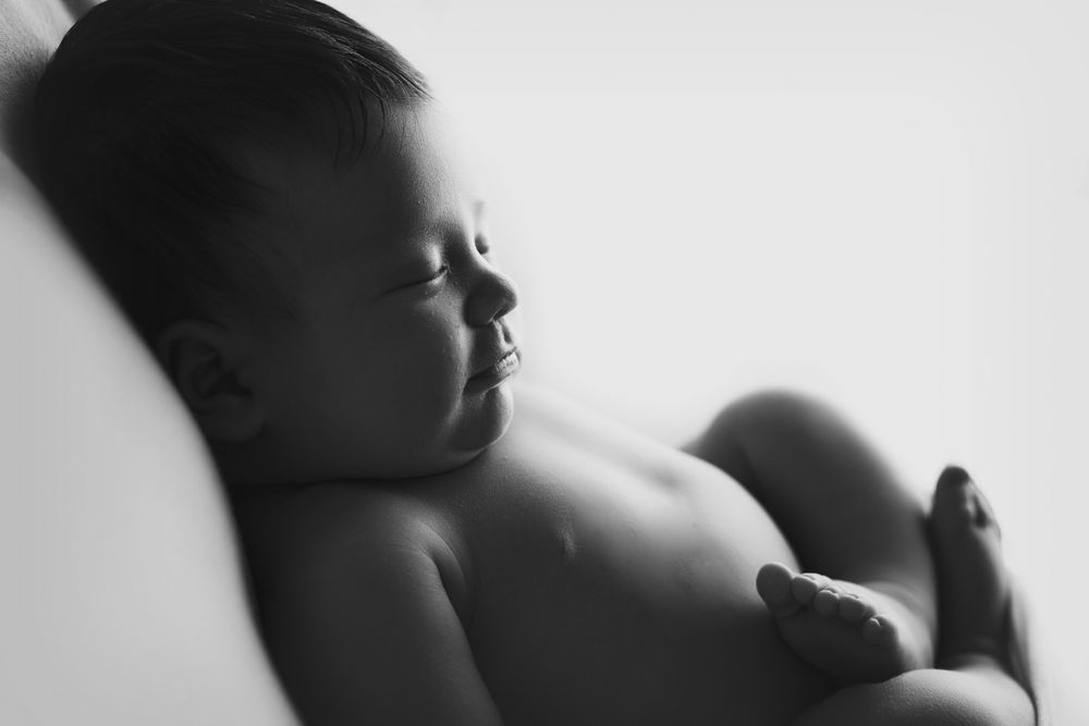 Black and white image of newborn baby girl backlit and profile of face.