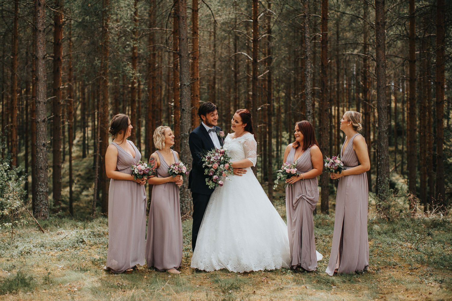 Brudfölje skrattar tillsammans med brudpar framför tallar i de Småländska skogarna i Tidersrum med soljus och dusty pink