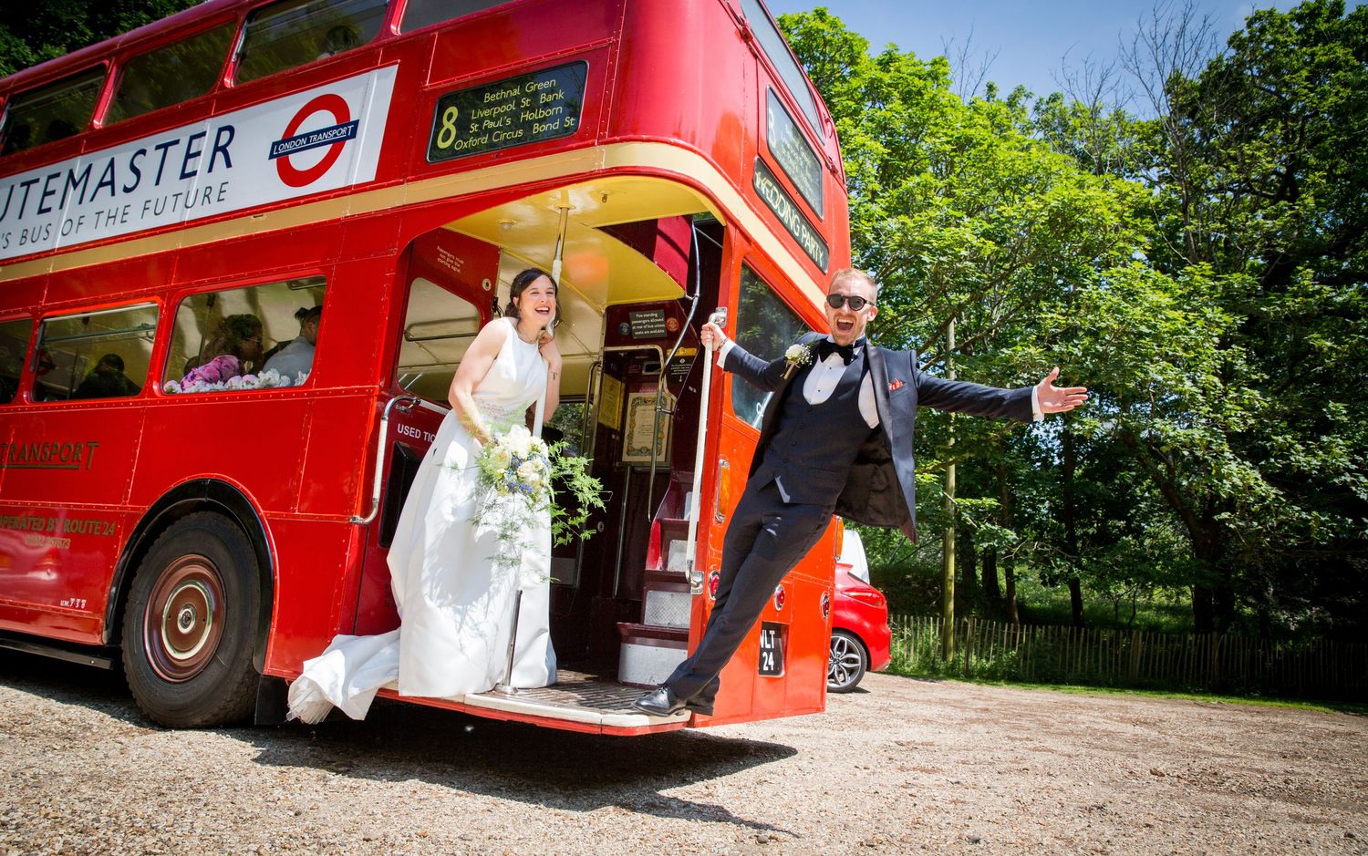 Red double decker bus serves as unique wedding transportation in a scenic outdoor setting.