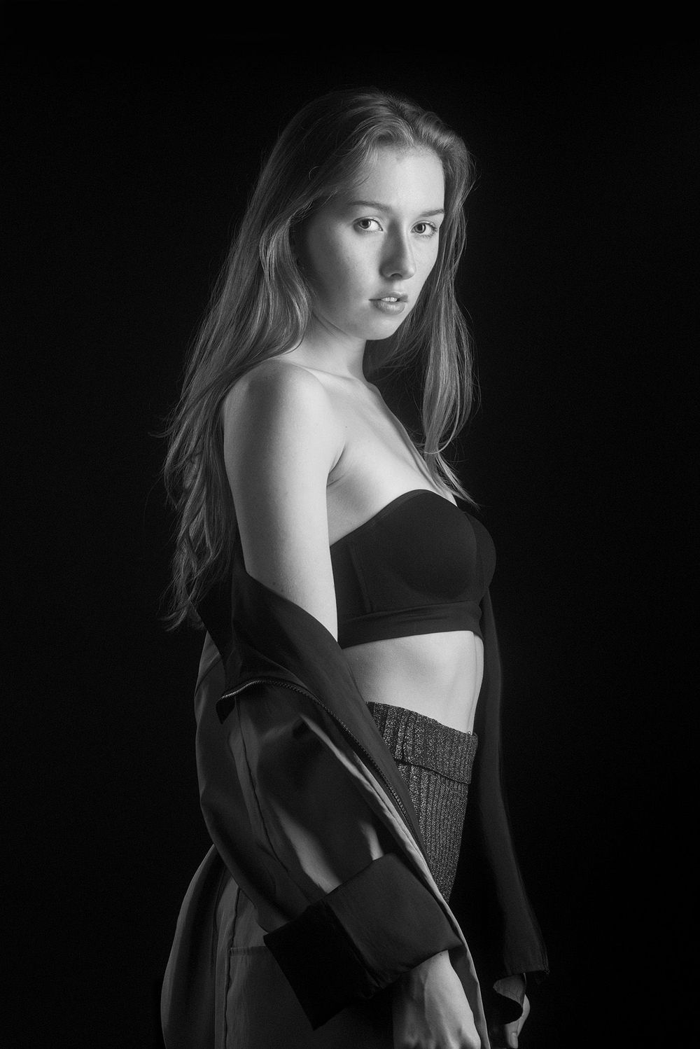 Black and white studio portrait of young blonde woman in strapless top and open jacket.