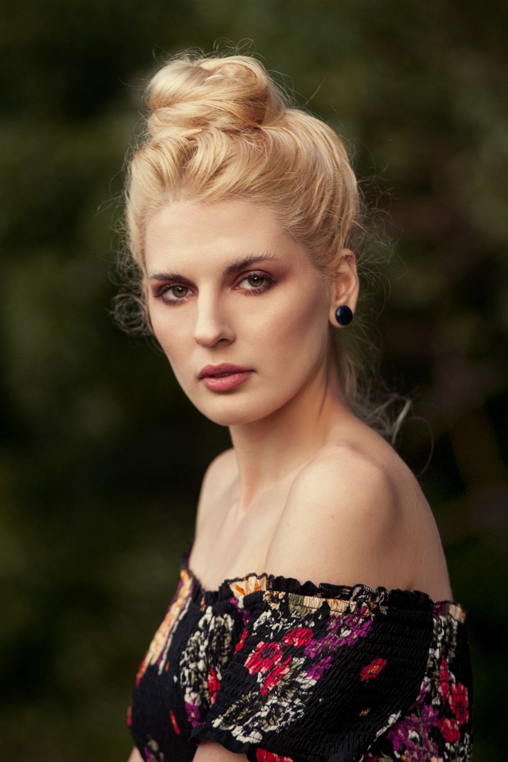 Blonde woman with hair bun in off-shoulder floral top in soft outdoor portrait.