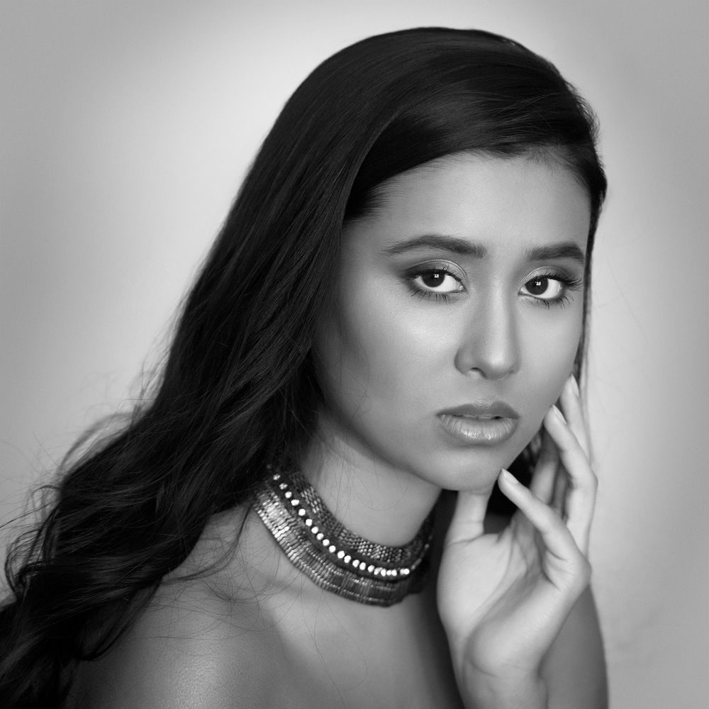 Black and white portrait of a young woman with dark hair wearing a statement necklace.