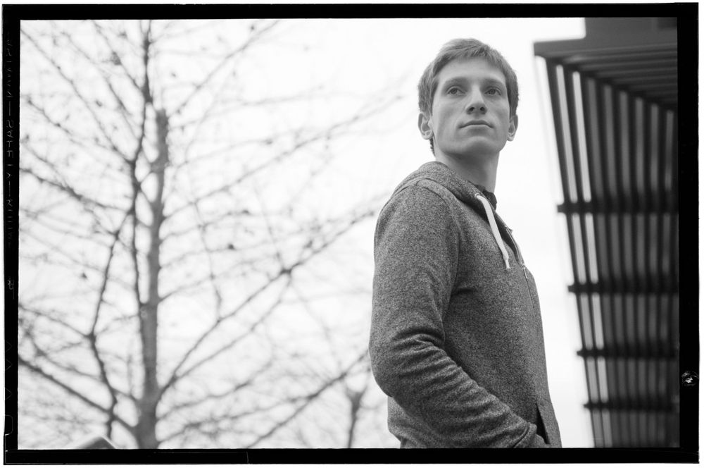 Young man in gray hoodie looking upward in moody black and white outdoor portrait.