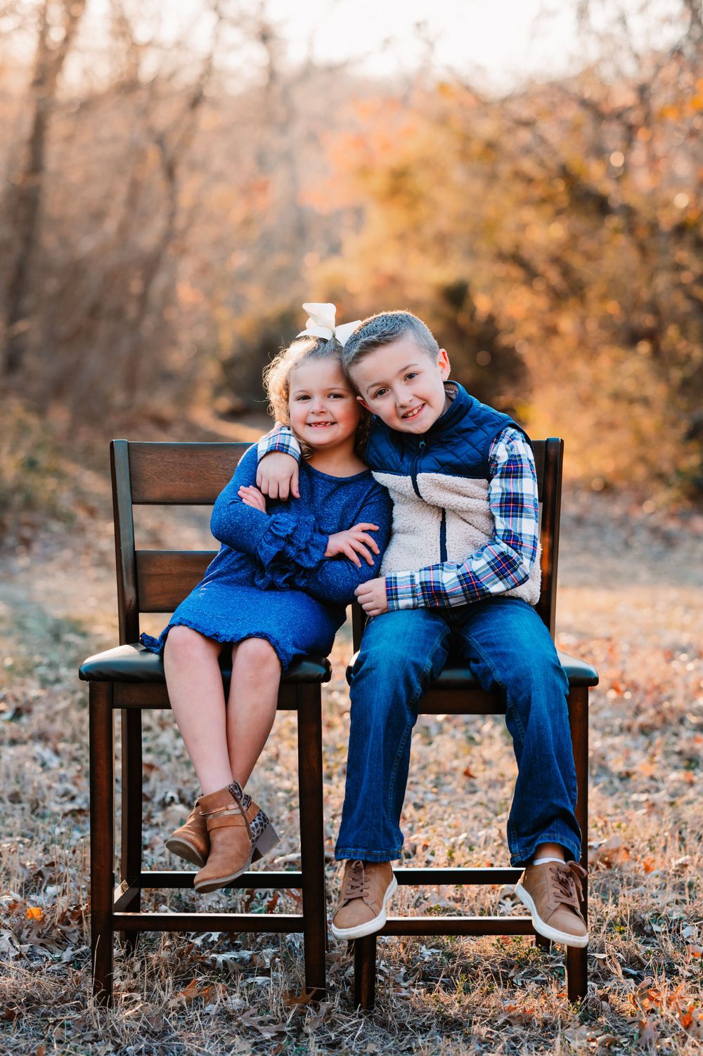 school aged siblings sit together in chairs during dallas area sunset extended family portrait session outdoors