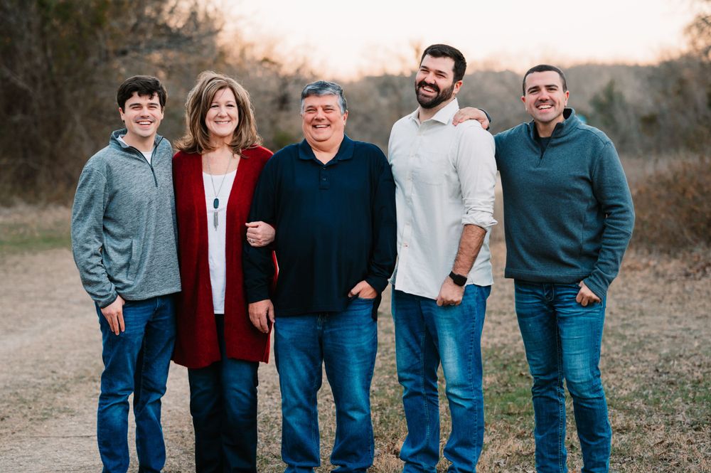 Couple with 3 adult children stand together during dallas area sunset extended family portrait session outdoors