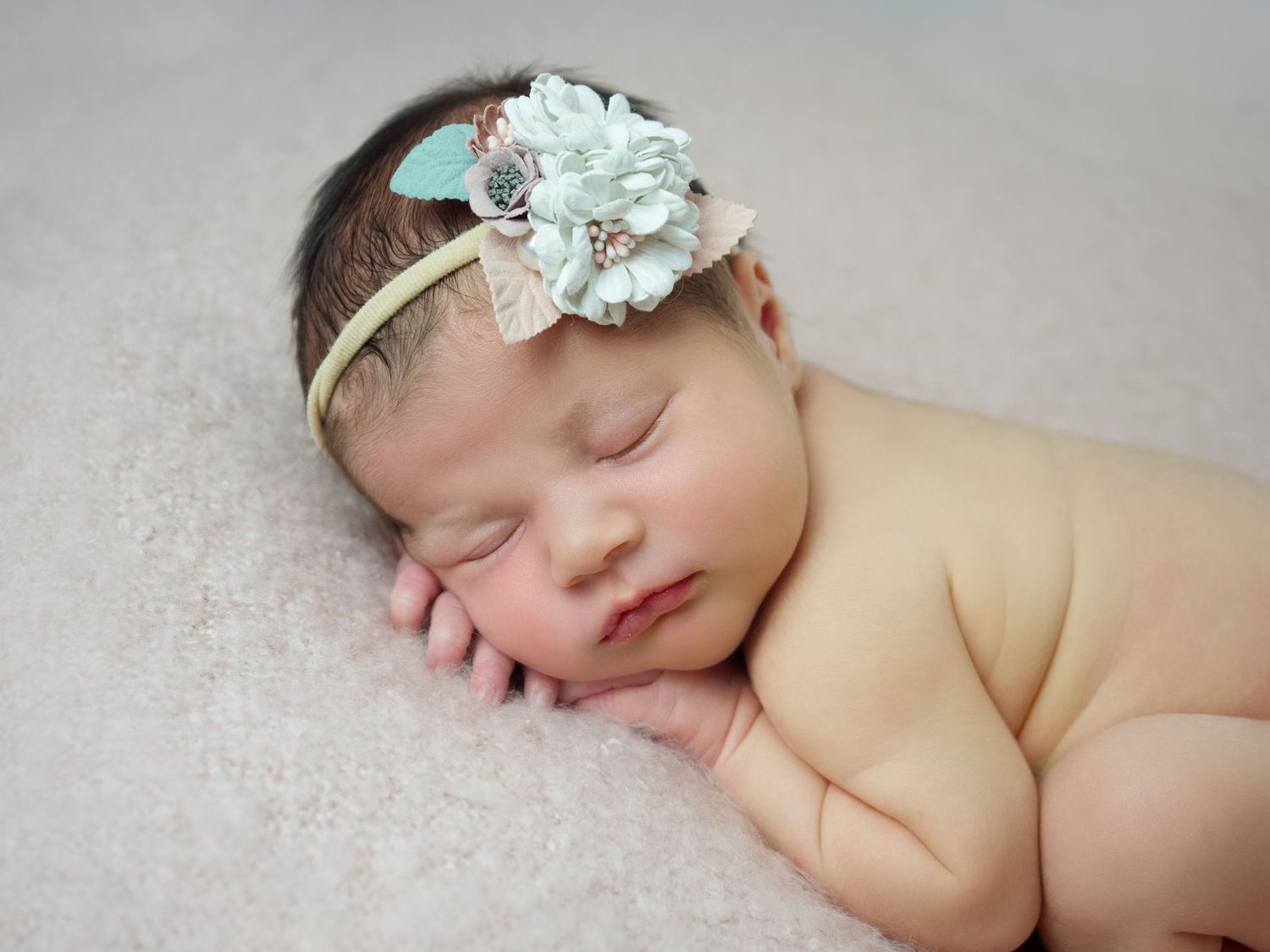 newborn baby girl with flower headband on a pink blanket