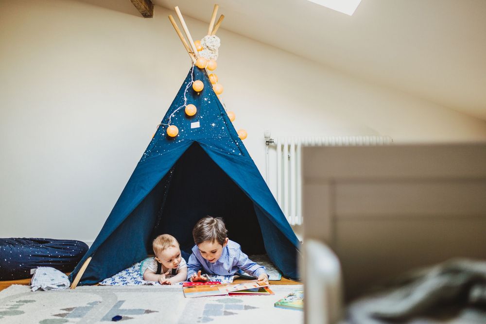 Blue teepee tent set up in a bright attic playroom with toys scattered around.