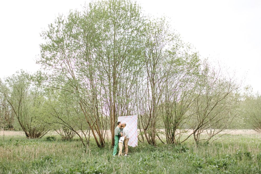 Natural outdoor maternity photoshoot in a green spring field with blooming trees.
