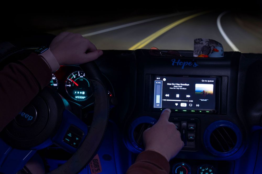 Driver using a car infotainment system at night with blue ambient lighting in the dashboard.