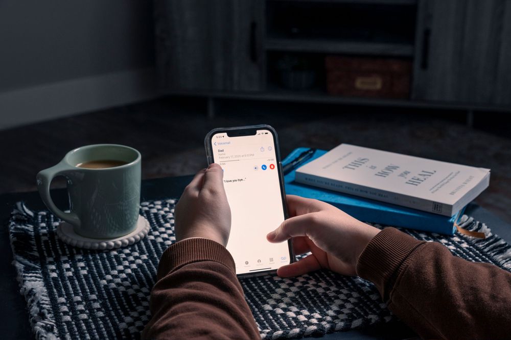 Hands holding smartphone with coffee cup and book on patterned blanket.