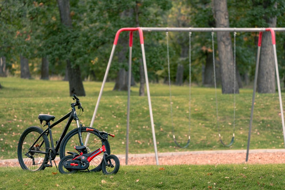 Bicycle parked near empty swing set in a green park.