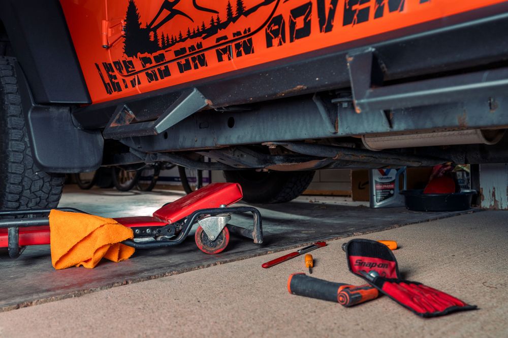 Red and orange tools scattered under a vehicle during maintenance.