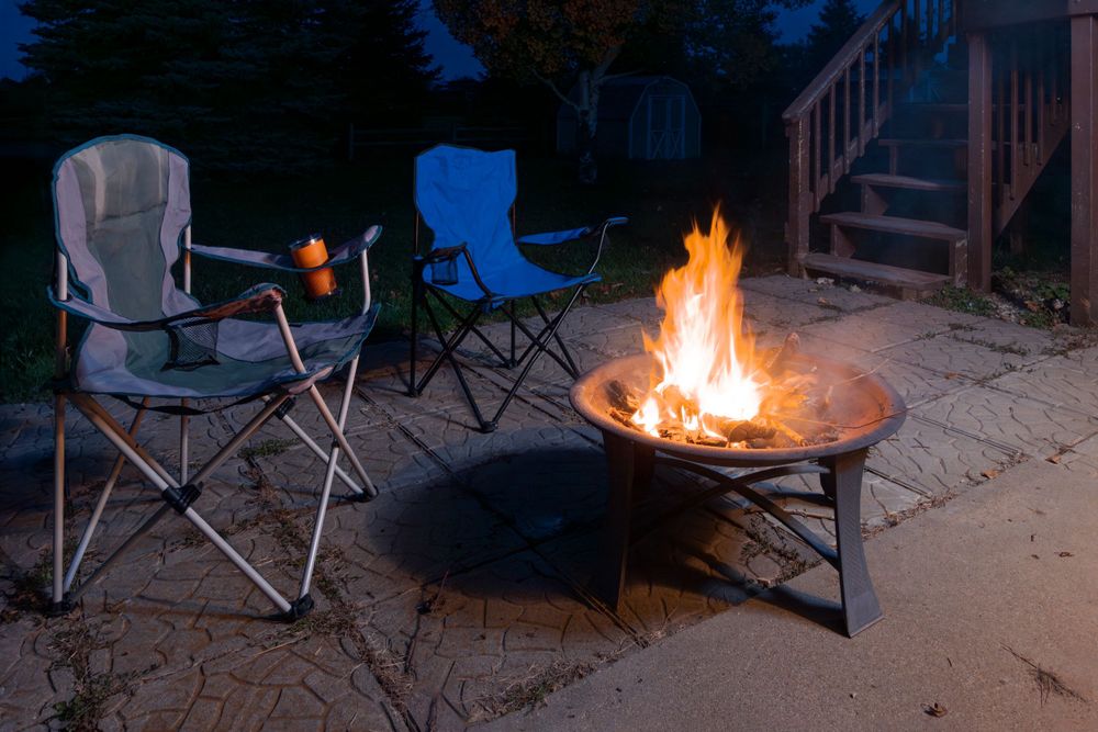 Outdoor gathering around a fire pit at night with camping chairs.
