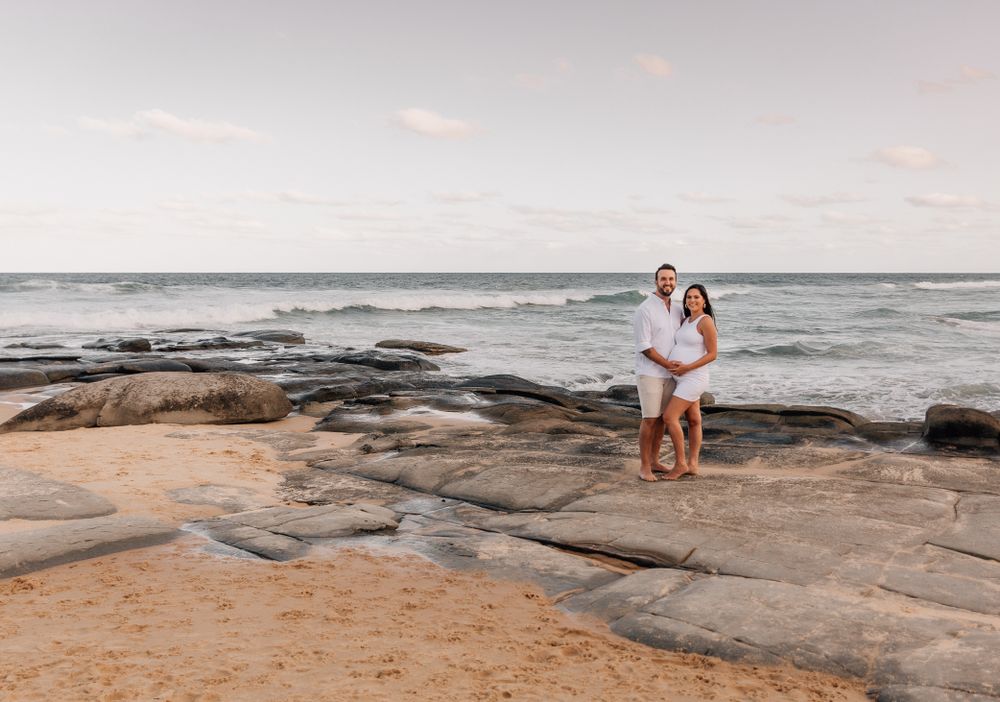Scenic coastal maternity photography session with rocks and ocean waves.