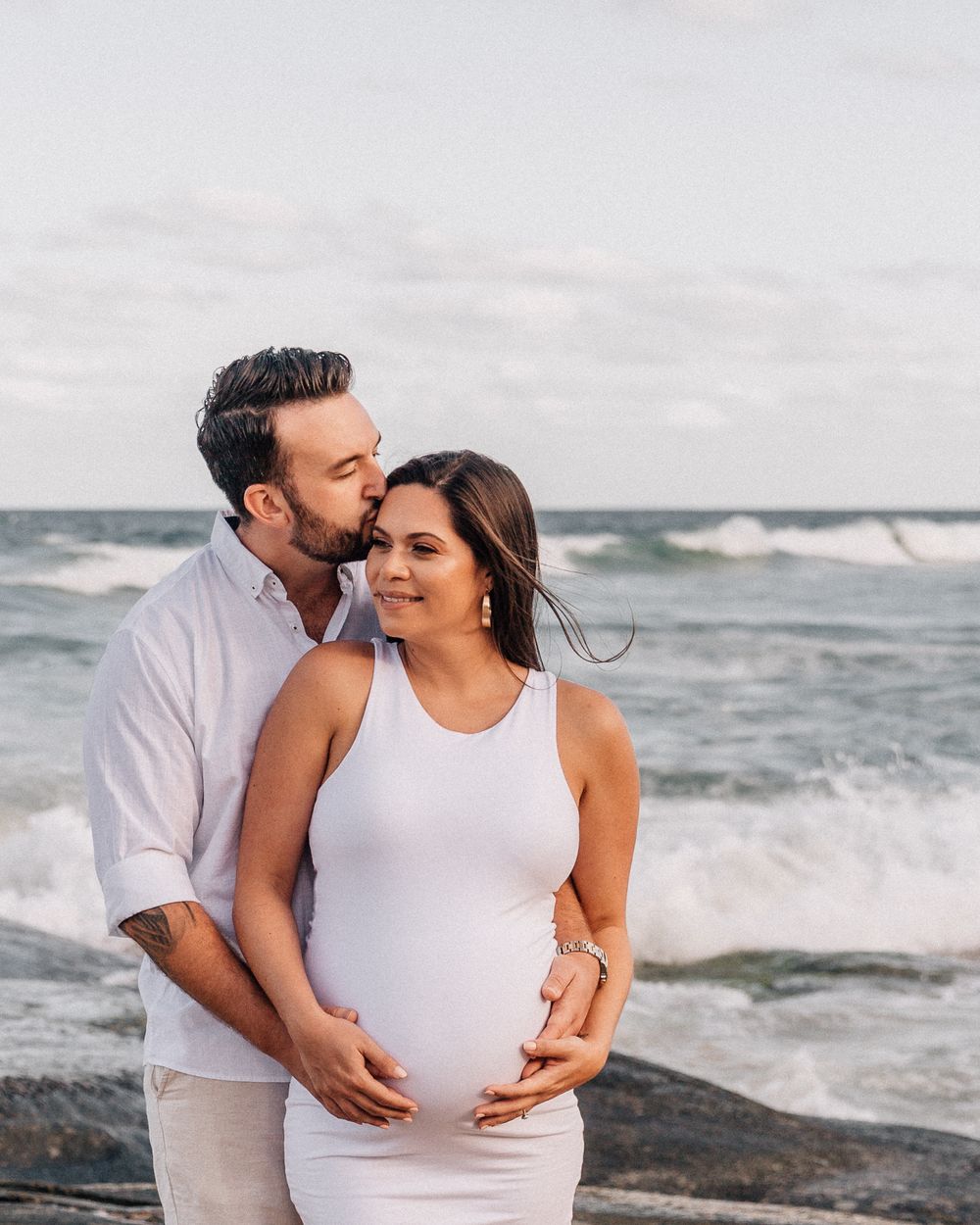 Intimate beach maternity photos with couple embracing against ocean waves.