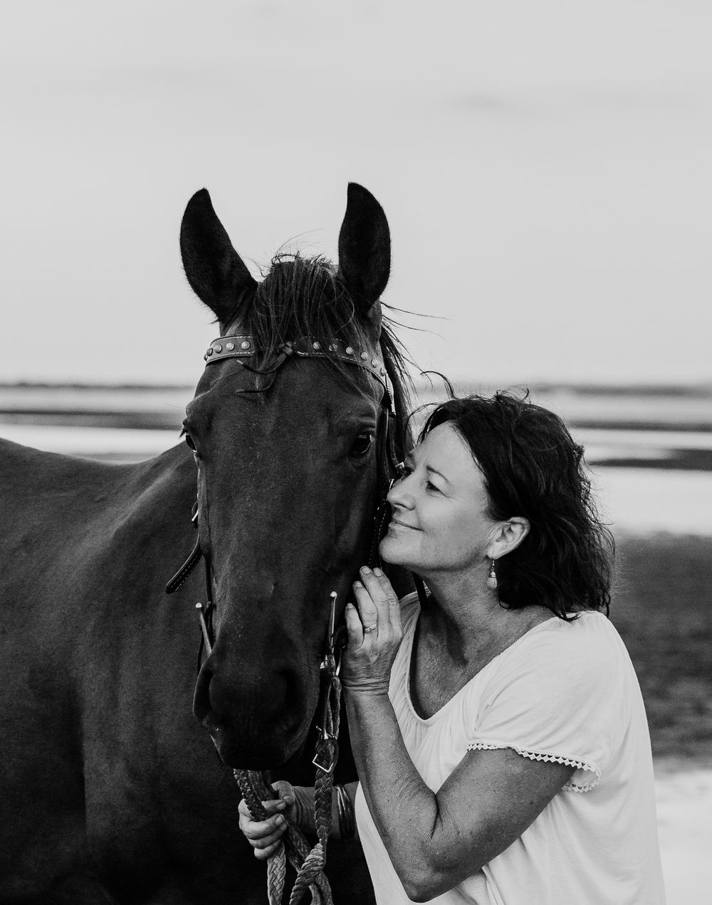 Black and white portraits of a woman bonding with her horse on the beach.