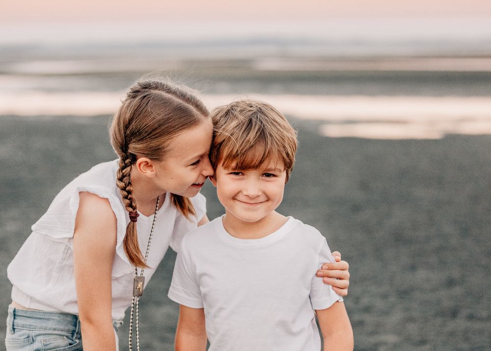 A sweet moment between two children sharing laughter on a coastal beach.