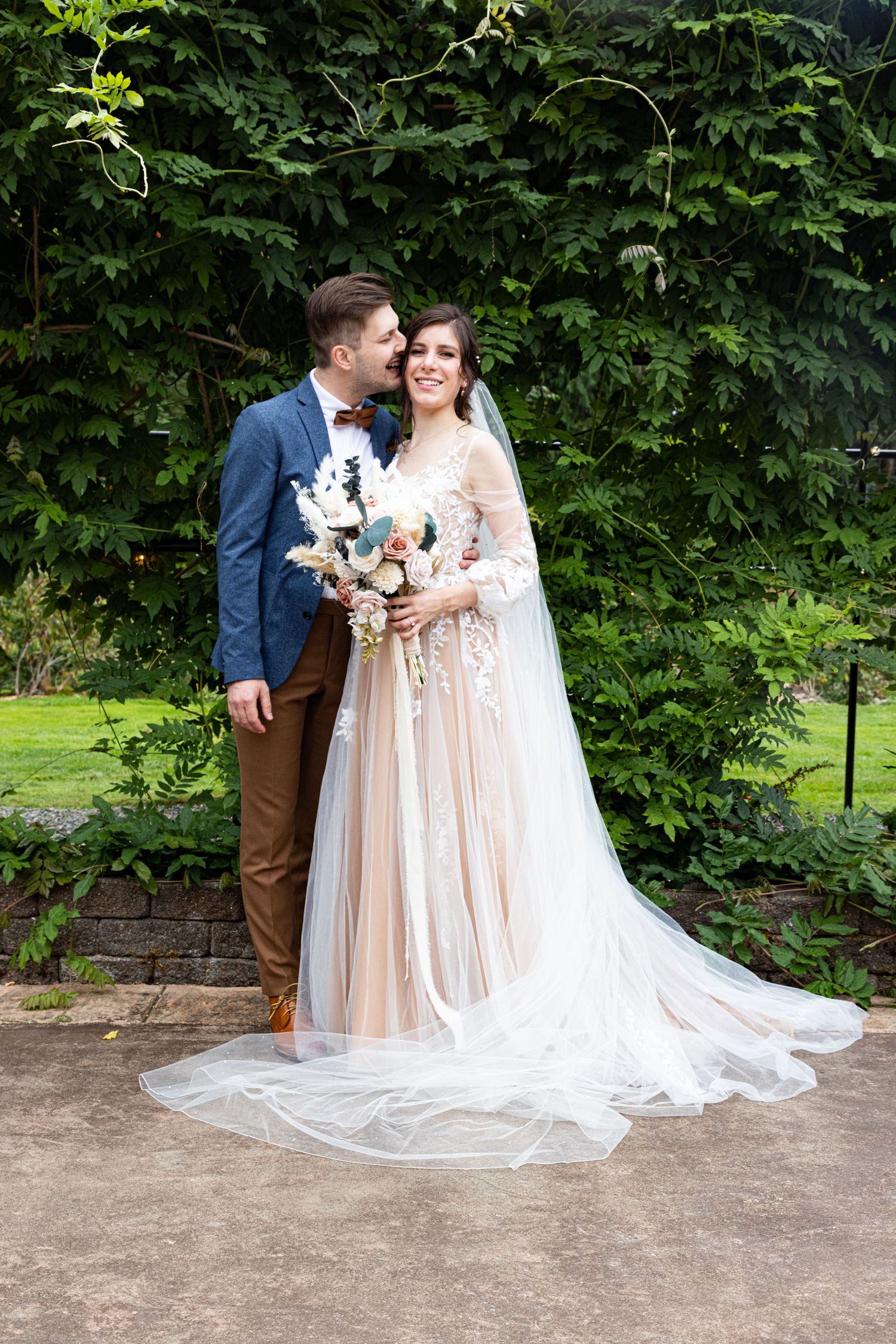A romantic outdoor wedding portrait with a bride in a flowing champagne gown and groom in navy.