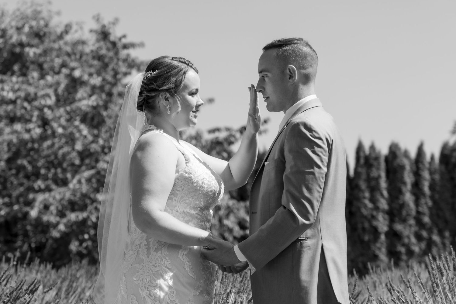Tender moment between newlyweds standing in front of evergreen trees during outdoor ceremony.