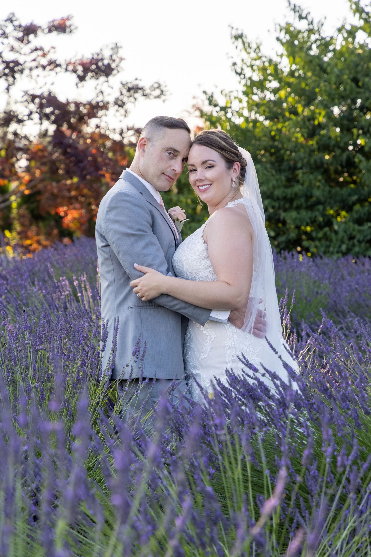 Couple poses together among purple lavender blooms during wedding photoshoot.
