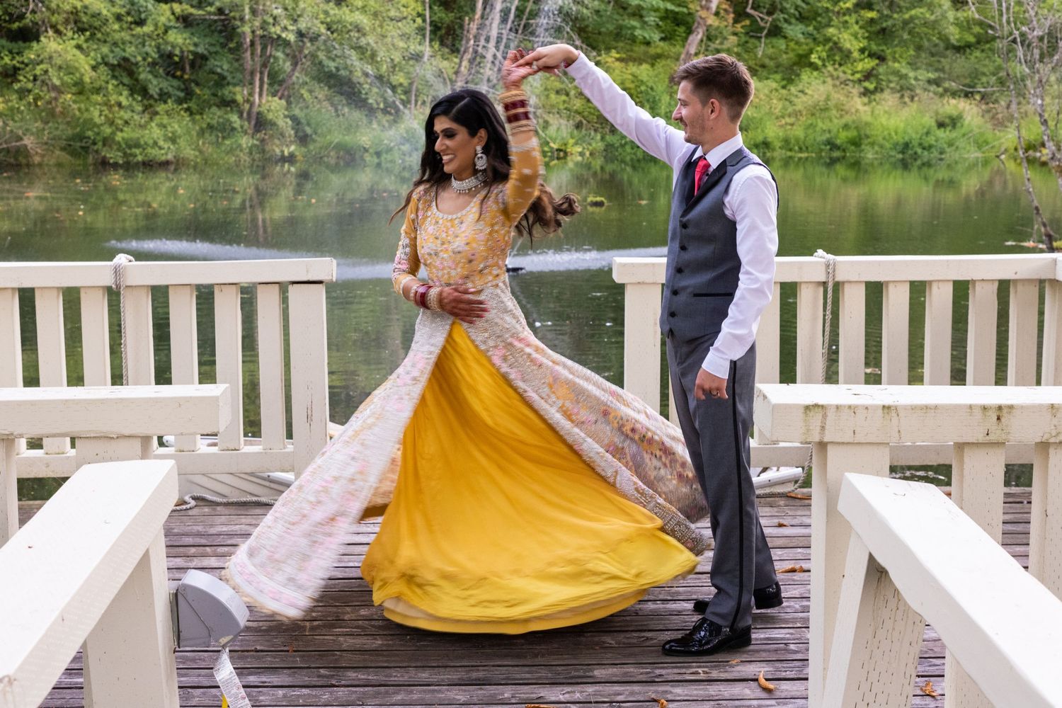 A couple dances on a wooden dock over a lake with the bride wearing a stunning yellow and white gown.