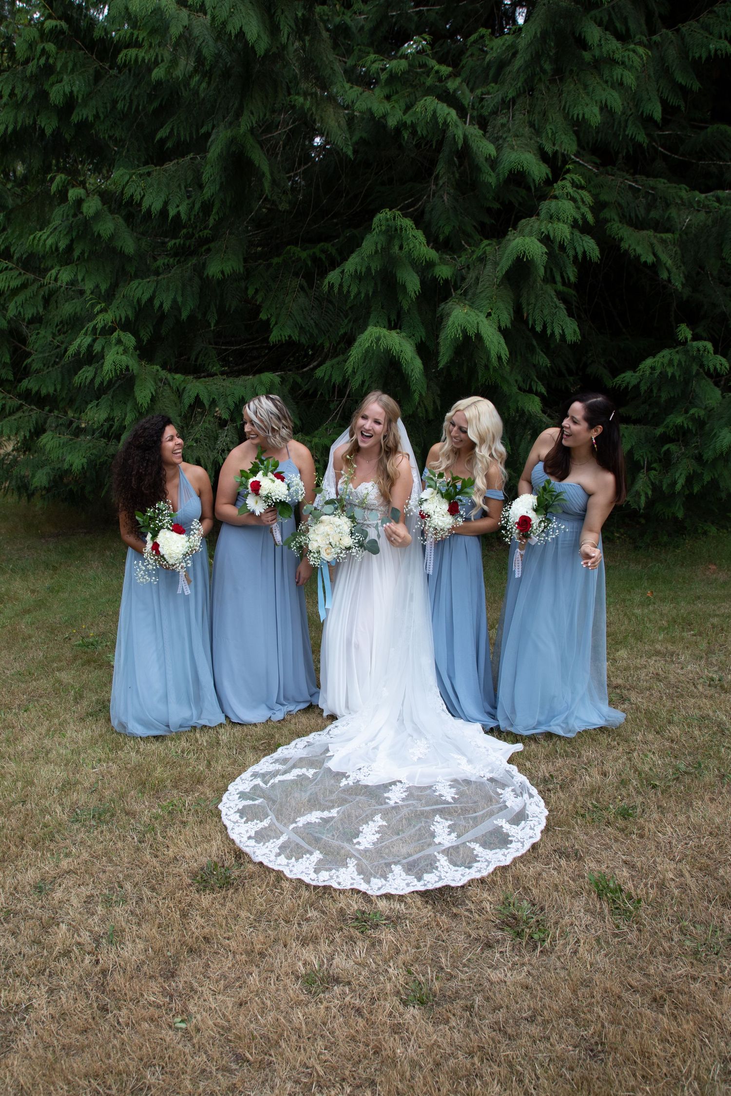 A bridal party in light blue dresses poses with the bride wearing a white gown with lace train.