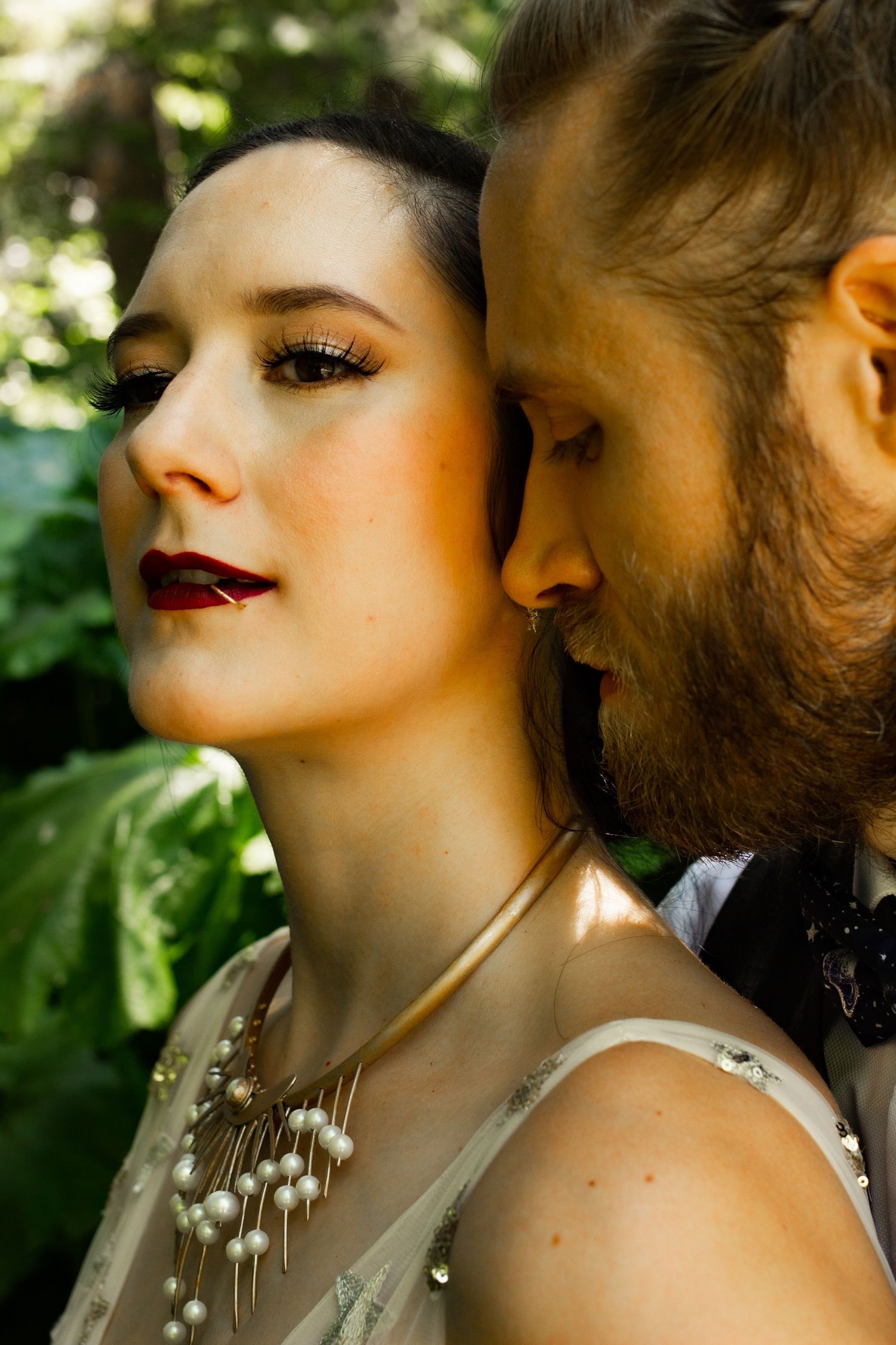 An intimate wedding portrait showing a couple in elegant formal wear against green foliage.
