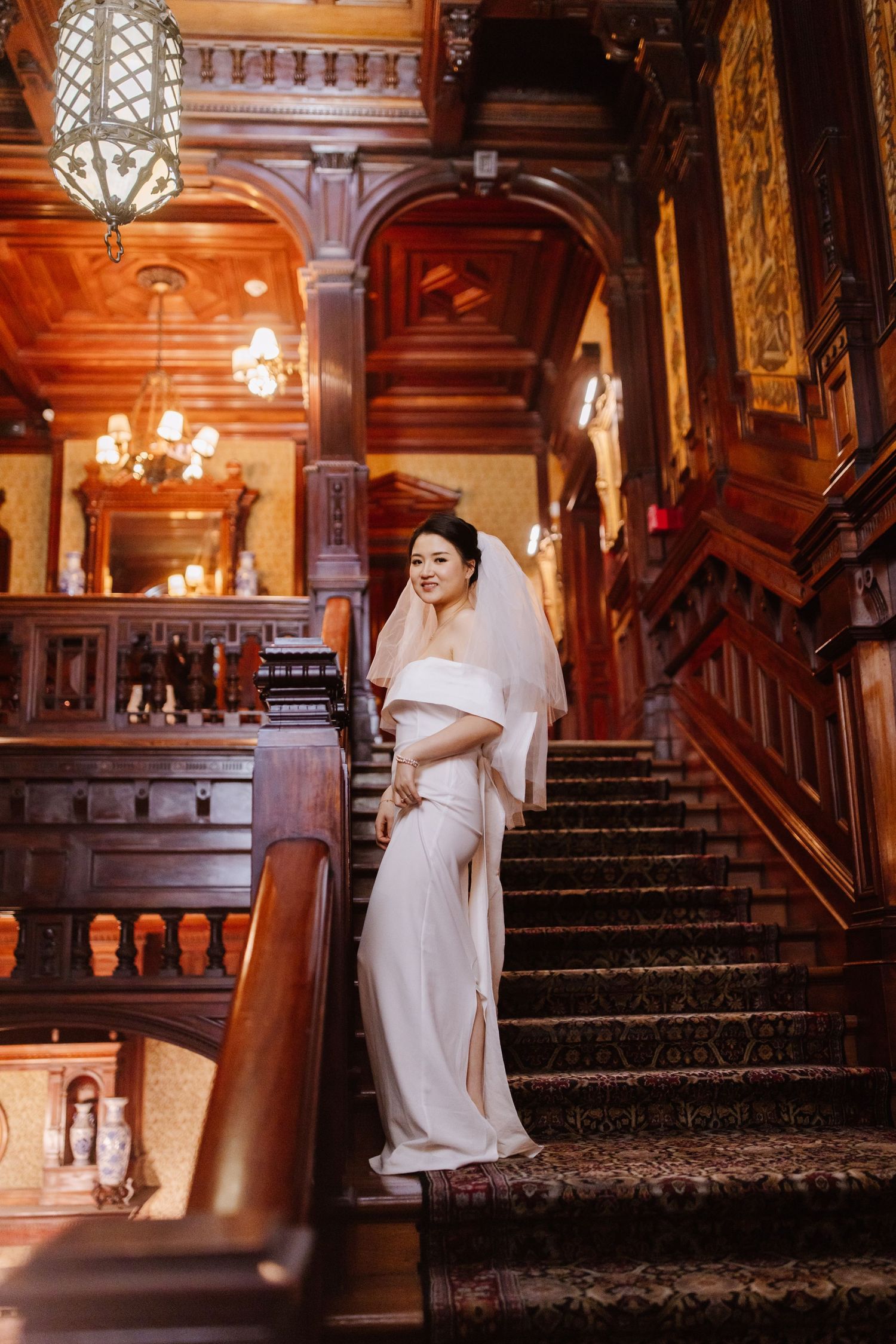 Bride in modern white dress posing on grand vintage staircase.