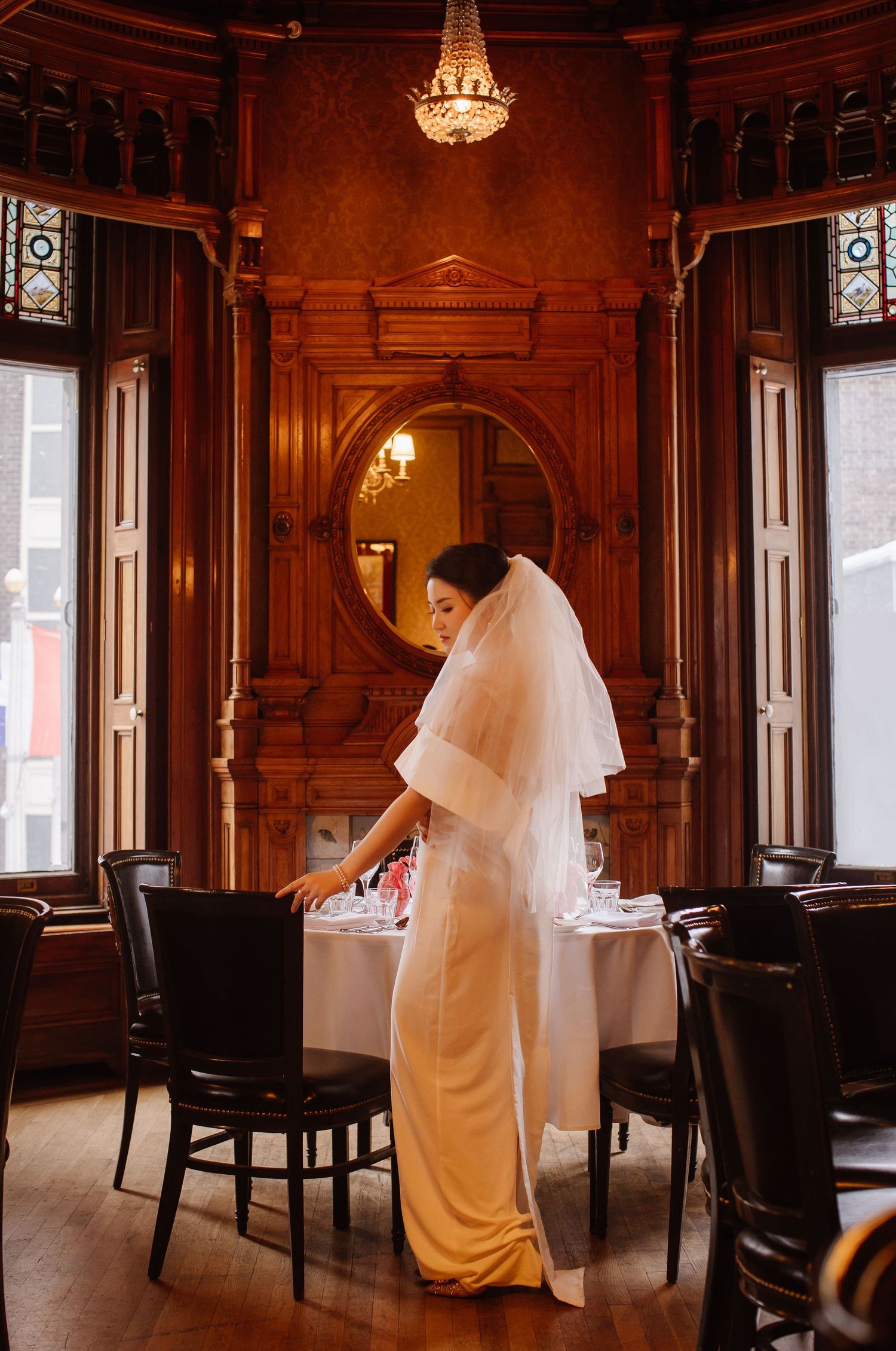 Wedding dress silhouette against elegant wooden paneled room with chandelier.